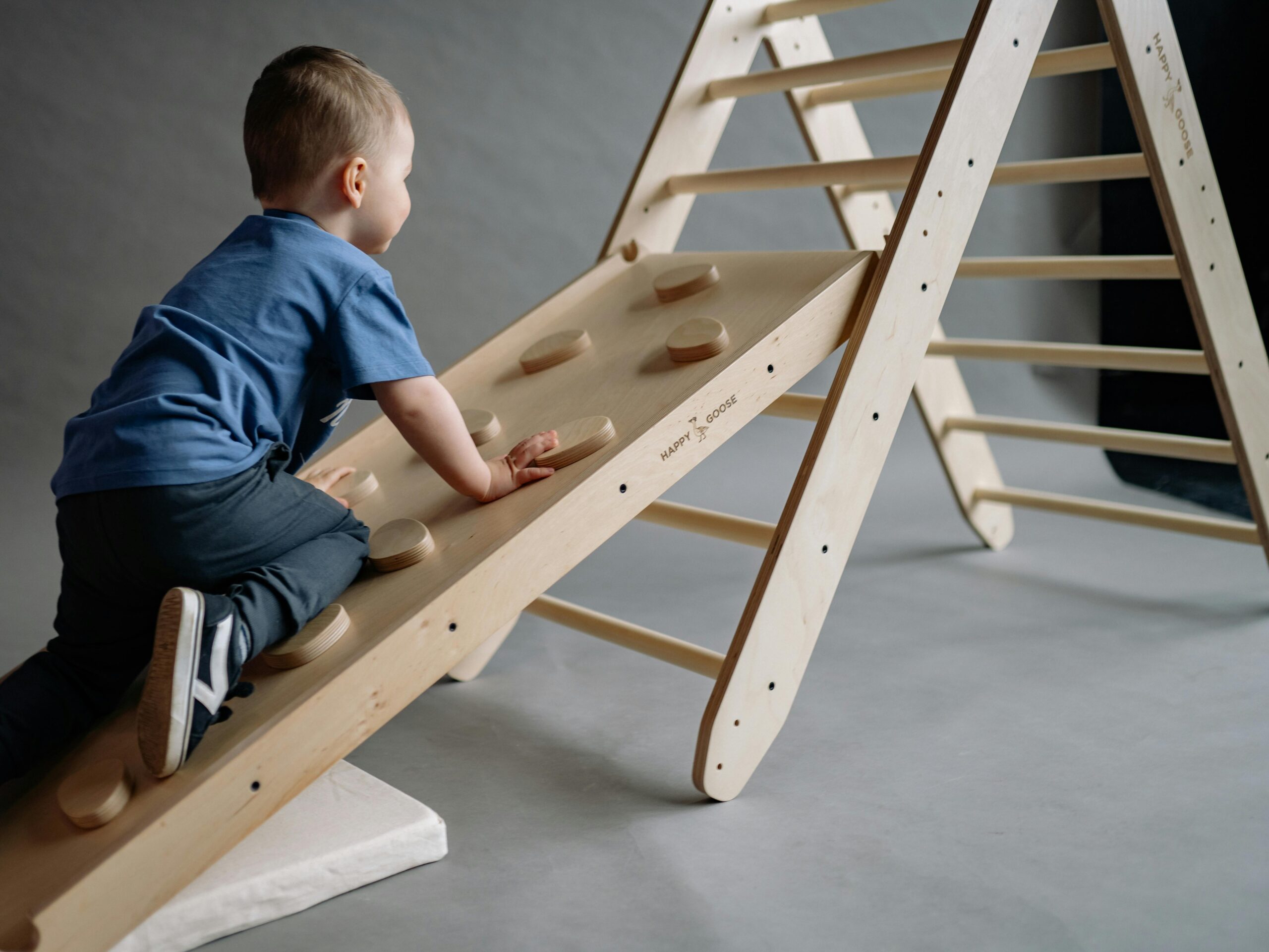 Gruba motorika A young boy enjoys playtime on a wooden indoor climbing set, combining fun and exercise.